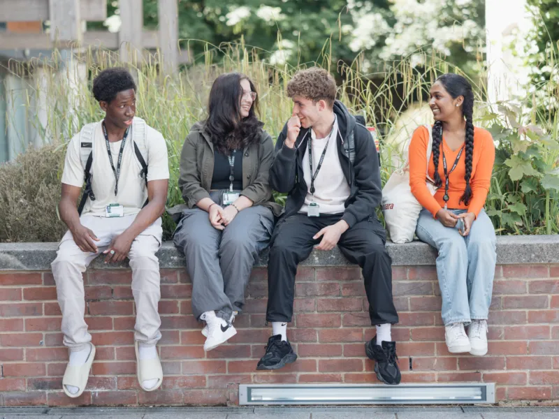 Four students sitting on a wall on campus.
