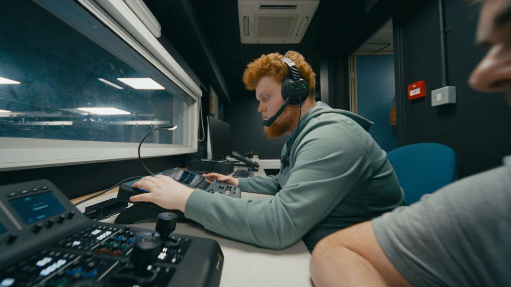 Student operating studio editing equipment in TV gallery.