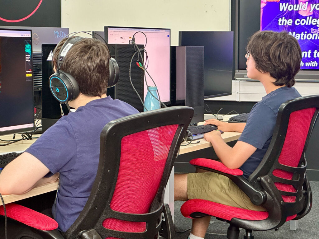 Student creating their Worldbuilder project sitting at desk with computers.