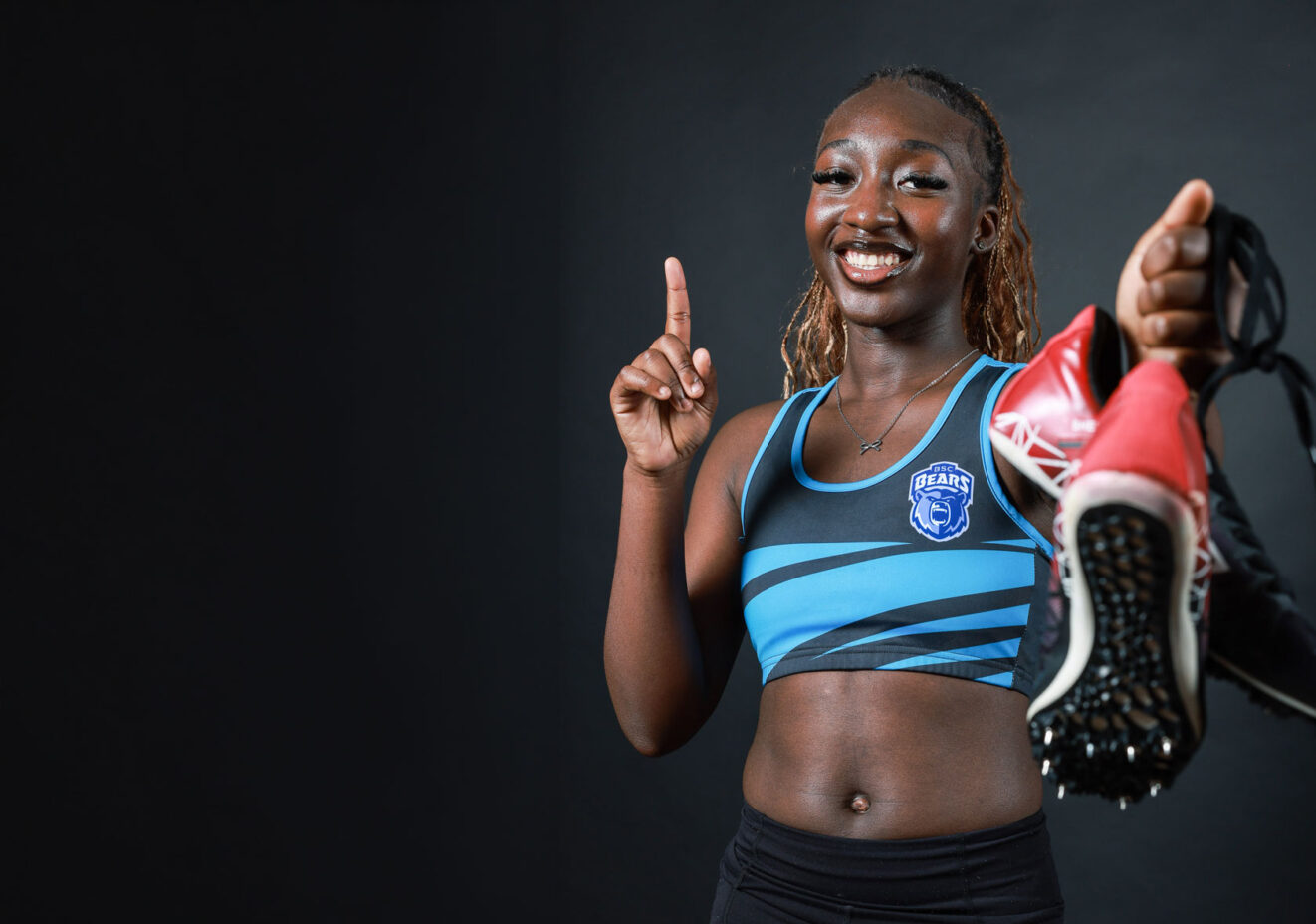 Female athlete holding running shoes, signalling number one with fore-finger.