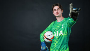 Men's football team goalkeeper holding football and pointing.