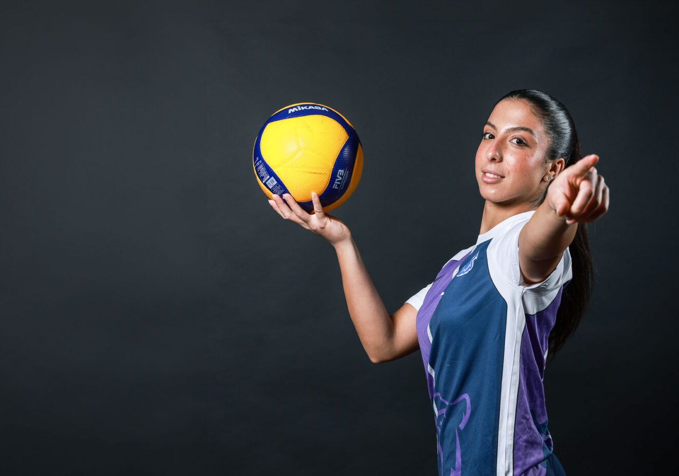 Volleyball player holding volleyball and pointing.