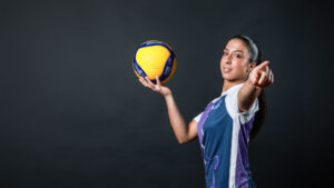 Volleyball player holding volleyball and pointing.